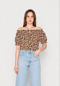 Top preto floral com ombros à mostra, mangas bufantes e detalhe de laço na frente, combinado com culotes de ganga azul claro de cintura alta.