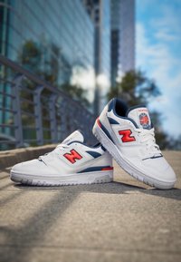 Vita sneakers med blå accenter och röd logotyp. Har perforerad design, vadderad tunga och mönstrad gummisula för bättre grepp.