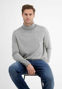 Szary sweter typu golf w miękkim, dzianinowym materiale, z prążkowanym kołnierzem i akcentem z logo. W połączeniu z niebieskimi dżinsami.