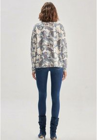 Helle Strickjacke mit Paisley-Muster in Blau und Rot, kombiniert mit dunkelblauen Jeans und knielangen Stiefeln, von hinten betrachtet.