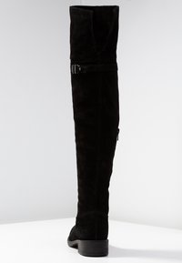 Stivale nero sopra il ginocchio in suede con una finitura liscia, dotato di una cinghia con accessori in argento e un tacco basso a blocco.