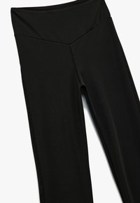 Schwarze Sportleggings aus glattem, dehnbarem Material mit hoher Taille, die an der Vorderseite eine V-förmige Naht aufweisen und ohne sichtbare Muster sind.