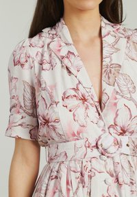 Abito floreale con bottoni in tessuto leggero, caratterizzato da fiori rosa e beige, maniche corte, vita con cintura e scollatura a V.
