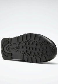 Suola di sneaker nera in gomma con scanalature profonde, caratterizzata da motivi circolari e a onda, e un logo impressa sulla mezze sole.