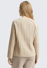 Beige geribbelde trui van zachte stof, met een ronde hals en lange mouwen in een ontspannen pasvorm. Geen zichtbare patronen of accenten.