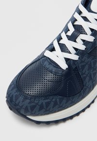 Marineblaue Sneaker mit einem perforierten Lederobermaterial, strukturierten Stoffbesätzen, weißen Schnürsenkeln und einer gemusterten Außensohle. Rund zulaufende Zehenpartie.