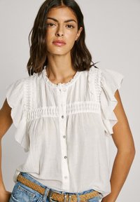 Weißes Bluse mit gerafften kurzen Ärmeln, die über Faltendetails und einen Knopfverschluss verfügt. Hergestellt aus leichtem Stoff mit strukturierter Oberfläche.