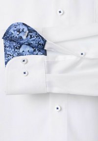 Witte overhemden met gestructureerde stof en een blauwe bloemen pochet. Heeft witte knopen met blauwe accenten en contrasterende manchetten.