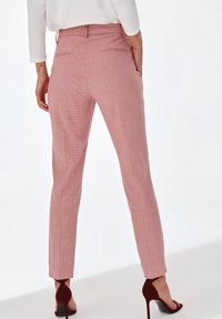 Pantalons à carreaux roses avec une coupe slim, dotés de deux poches arrière. Le matériau semble lisse et ils sont associés à des chaussures à talons rouges.