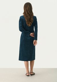 Langärmliges, dunkelblaues Cordkleid mit tailliertem Oberteil und gerader Rockform. Verfügt über eine Rückennaht-Detaillierung und eine subtile Textur.
