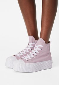 Höga sneakers i ljusrosa kanvas, med vita snörningar och gummisålar med texturerade detaljer, rundad tå och ribbad plattform.