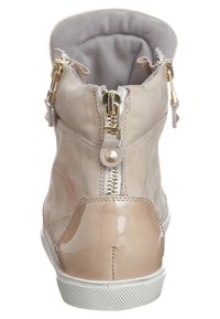 Beige ankle boot with glossy patent accents, dual gold zippers at the rear, a textured sole, and a soft, light gray lining.