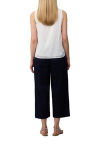 Weißes ärmelloses Oberteil mit strukturiertem Wellenmuster, kombiniert mit navy blauen weit geschnittenen Hosen. Sandalen mit Riemen vervollständigen das Outfit.