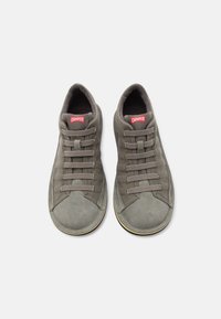 Ζευγάρι γκρι αθλητικών παπουτσιών Camper με φαρδιές, επίπεδες κορδόνια, σουέτ καλύμματα στα δάχτυλα και κόκκινο λογότυπο Camper στη γλώσσα, σε άποψη από πάνω, σε λευκό φόντο.