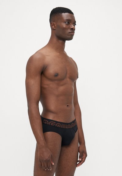 Schwarze Baumwollslips mit einem gemusterten, elastischen Taillenbund, der ein kontrastierendes Design aufweist. Glatte Textur und figurschmeichelnde Form.