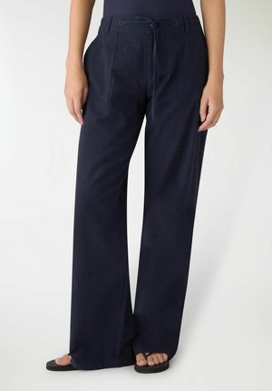 Donna che indossa pantaloni ampi navy con tasche frontali e vita con coulisse, abbinati a sandali infradito neri.