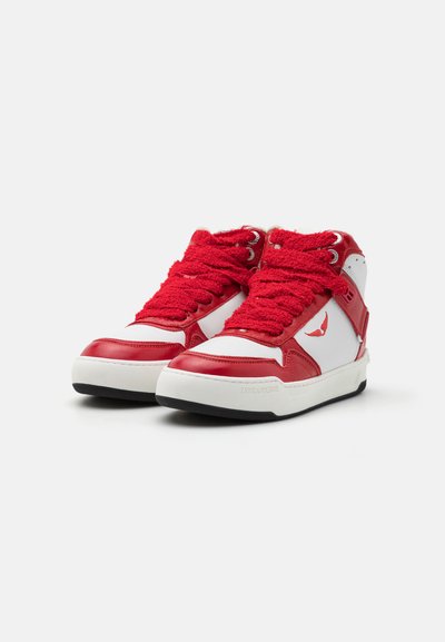 Red and white high-top sneakers with textured red laces, smooth leather body, patterned accents, and a black rubber sole.