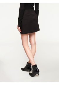 Černá minisukně se bočními kapsami, vyrobená z hladké tkaniny. Kombinována s černými koženými kotníkovými botami s špičatou špičkou a nízkým podpatkem.