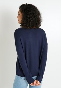 Suéter de manga larga azul marino con un corte relajado y dobladillo acanalado. Presenta un escote amplio y hombros caídos, fabricado en material de punto suave.