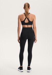 Czarny stanik sportowy z designem racerback oraz wycięciem w kształcie klucza, w połączeniu z czarnymi legginsami o wysokim stanie. Gładka tekstura, odpowiednia do odzieży sportowej.