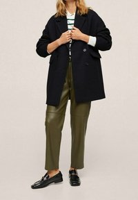 Tuplarivinen laivastonsininen takki yläosaltaan väljähkössä istuvuudessa, yhdistetty oliivinvihreisiin keinonahkahousuihin ja mustiin loafer-kenkiin. Sisällä valkoinen ja vihreäraidallinen paita.