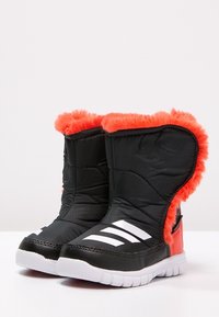 Czarne zimowe botki z pomarańczowym sztucznym futerkiem, pikowanym wykończeniem i białymi paskami po bokach. Gumowa podeszwa z teksturą antypoślizgową.