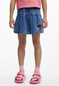 Denim suknja ima lepršav kroj s nabranojinki, plave boje i vezenu šarenu dekoraciju na rubu. Nosila se s ružičastim sandalama.