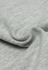 Svetle šedá látka s hladkým, jemným povrchem. Materiál vykazuje drobné variace v odstínu a jemný pletený vzor.