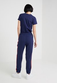 Camiseta de algodón azul marino combinada con joggers azul marino que cuentan con rayas laterales rojas y una cinturilla elástica. Zapatillas blancas completan el conjunto.