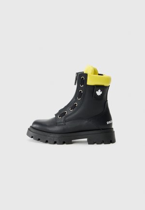 Bottines noires en cuir avec un col jaune, quincaillerie argentée et une semelle en caoutchouc épaisse. Présente un logo en forme de feuille et un détail de fermeture éclair à l'avant.