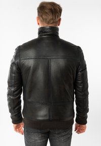 Chaqueta de cuero negra con un cuello alzado, puños acanalados y dobladillo. Presenta costuras en la parte posterior y en los hombros. Textura suave.