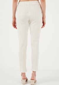 Creme broek met elastische tailleband en subtiele verticale strepen, aansluitende pasvorm en een gladde textuur, gecombineerd met lichtgekleurde haksandalen.
