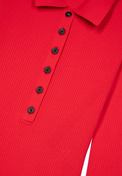 Rød rippet poloshirt med en krave, der har sorte knapper og en lille broderet logo på venstre side.