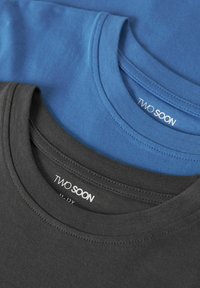 To sammenbrettede crew-neck T-skjorter i blått og koksgrått, med merkeetiketten "Two Soon" synlig på innsiden av kragen.