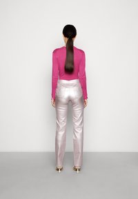 Fin snugly långärmad rosa topp, kombinerad med glänsande silverfärgade högmidjade byxor. Bakvyn visar en slät tyg och rakt ben med diskreta fickor.