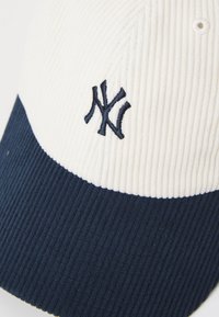 White and navy corduroy cap with ribbed texture, featuring an embroidered logo on the front. Distinct color blocking design.