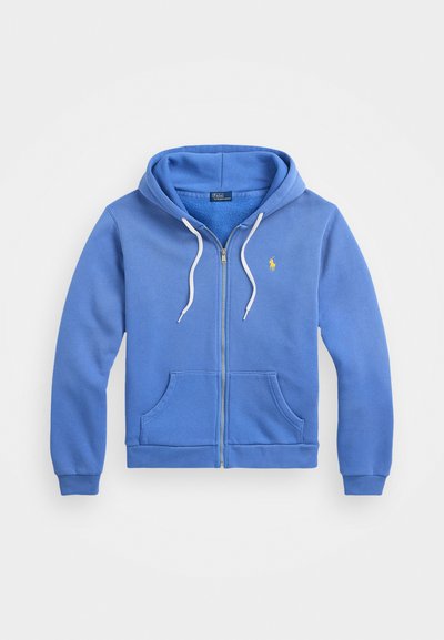 Blå hettegenser med glidelås laget av mykt stoff, med en frontlomme, hvite snorer og en liten gul logo på brystet.