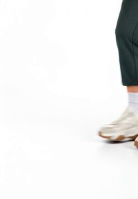 Persoană care poartă pantaloni negri, șosete albe și pantofi sport albi, mergând pe un fundal alb.