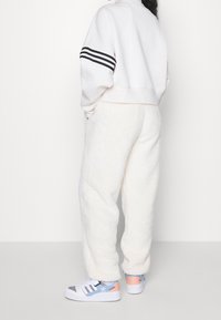 Valkoiset fleece-housut, joissa on teksturoitu pinta, yhdistettynä vaaleanharmaaseen lyhytseläiseen collegepaitaan, jossa on kolme mustaa raitaa yhdellä hihalla, sekä sinisin yksityiskohdin varustettuihin lenkkareihin.