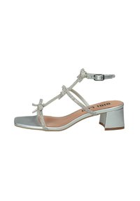 Sandalo argentato con cinturini e punta quadrata, con tacco basso a blocco. Caratterizzato da fiocchi decorativi e chiusura con fibbia. Materiale sintetico liscio.