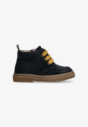Stivale alla caviglia in suede nero con suola spessa marrone e tre lacci gialli, cerniera laterale e linguetta sul tallone.