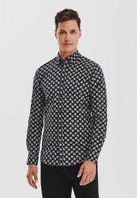 Granatowa koszula z guzikami z białym okrągłym wzorem, długimi rękawami, kołnierzykiem z ostrymi końcami i prostym dołem. Gładka tekstura materiału.