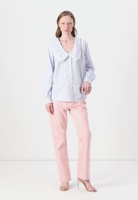 Camicia button-down a righe azzurre con un grande colletto bianco, abbinata a pantaloni dritti rosa e sandali con tacco beige.