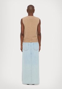 En lys beige strikket ermeløs topp kombinert med et lyseblått, langt denimskjørt med to baklommer og en rett silhuett.