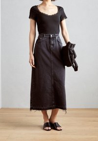 Top negro con encaje, combinado con una larga falda de mezclilla en gris oscuro, que presenta un dobladillo sin rematar y botones frontales. Sandalias deslizantes negras completan el look.