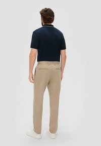 Granatowa koszulka polo z krótkim rękawem oraz jasnobeżowe spodnie. Spodnie mają kieszenie z guzikowymi akcentami. Białe trampki dopełniają strój.