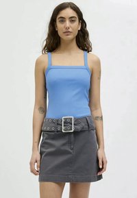 Top de alças azul com decote quadrado, combinado com uma saia de ganga cinza com uma grande fivela e ilhós.