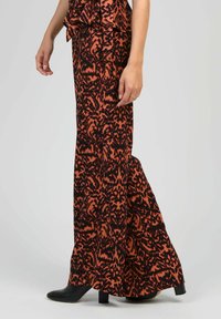 Pantalons longs et fluides avec un motif abstrait orange et noir, fabriqués à partir d'un tissu doux, avec une silhouette évasée et un léger éclat.
