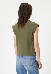 Oliven grøn, ribbet crop top med korte ærmer, der har en afslappet pasform og rund halsudskæring. Sammen med lyseblå højhusede jeans.