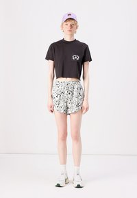 Black cropped t-shirt with a front pocket, paired with high-waisted shorts featuring a black and white abstract pattern. Accessories include a lilac cap.